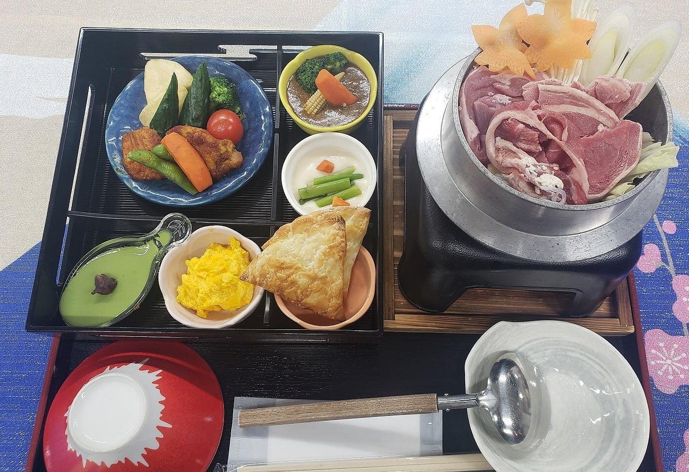 Japanese set lunch on a black tray, with a hot pot of sliced meat and vegetables beside small side dishes